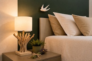Ein ordentlich bezogenes Bett mit weißem Kopfteil, eine Nachttischlampe mit Holzfuß und ein kleiner Blumentopf auf dem Nachttisch.