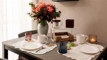 Une table à manger dressée avec des assiettes, des tasses, une cafetière, une bougie et un vase rempli de fleurs.