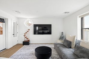 Un salon moderne avec un téléviseur à écran plat fixé au mur, une table basse noire, un canapé gris agrémenté de coussins et un élément décoratif mural.