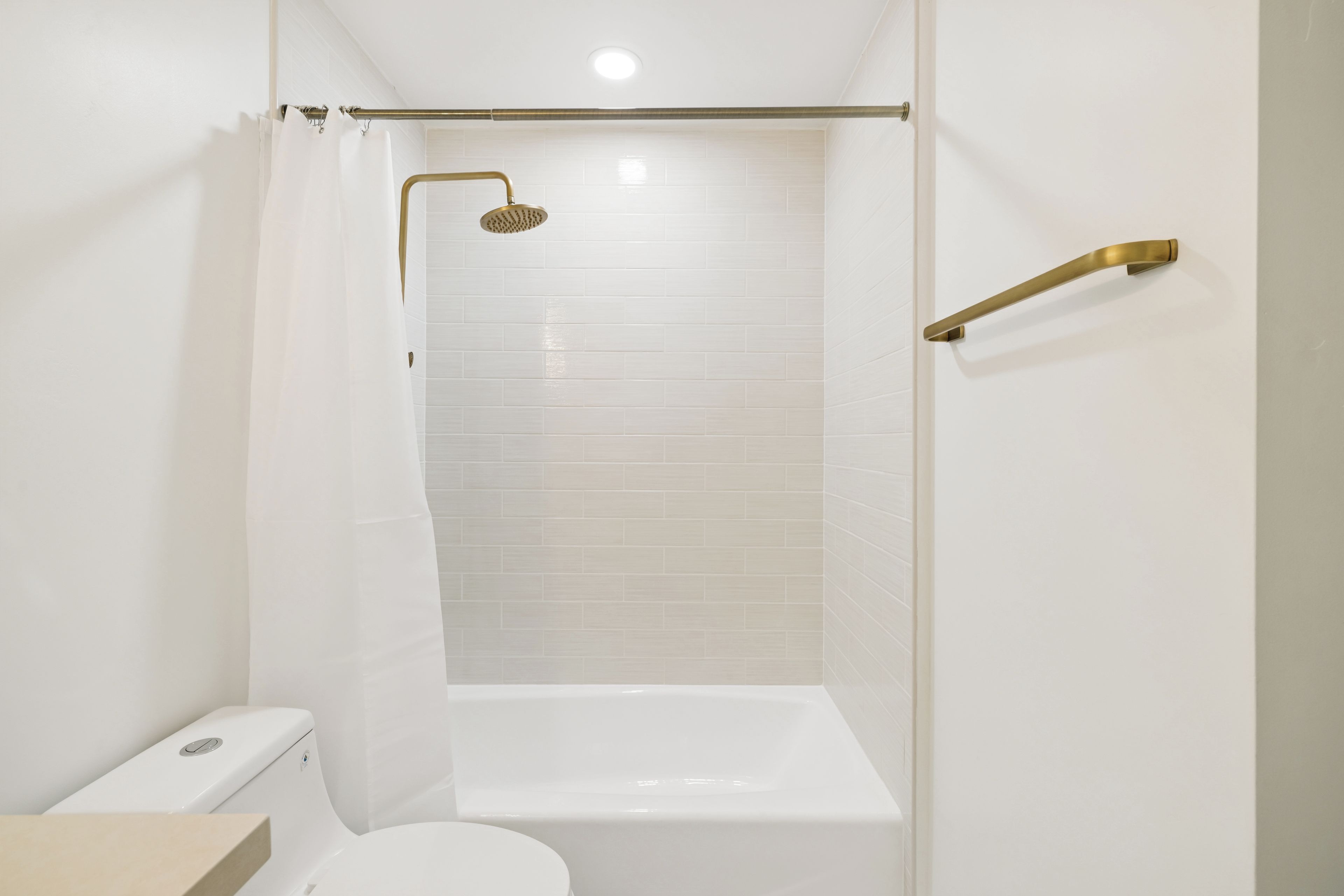 A bathroom with a white toilet, a bathtub, and a shower with a gold showerhead.