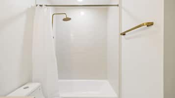 A bathroom with a white toilet, a bathtub, and a shower with a gold showerhead.