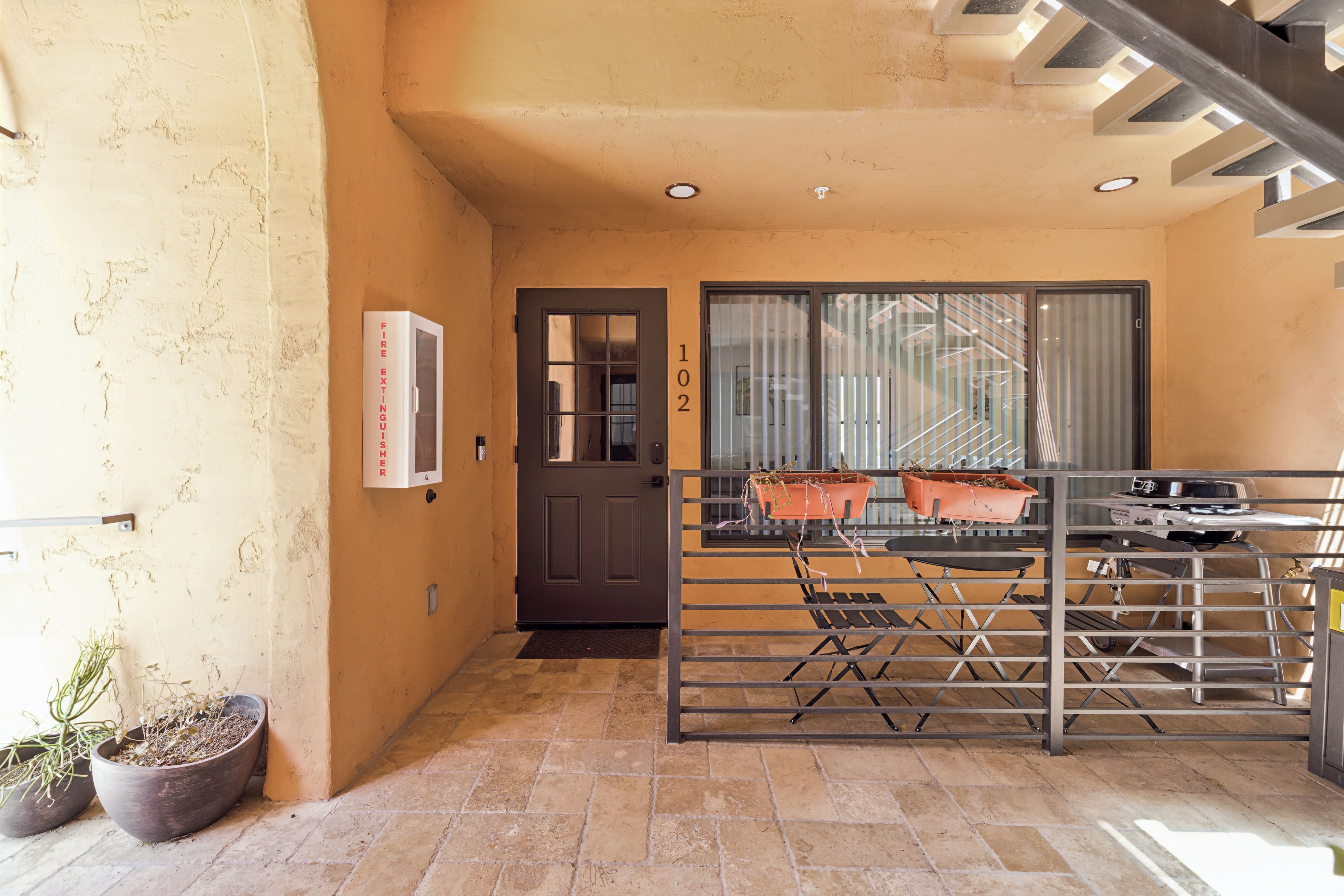 A compact entryway with a dark door, a fire extinguisher mounted on the wall, and a number '102' above the door.