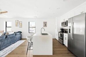 Une cuisine moderne dotée d’un îlot central, d’appareils électroménagers en acier inoxydable et offrant une vue sur la rue grâce à ses fenêtres.