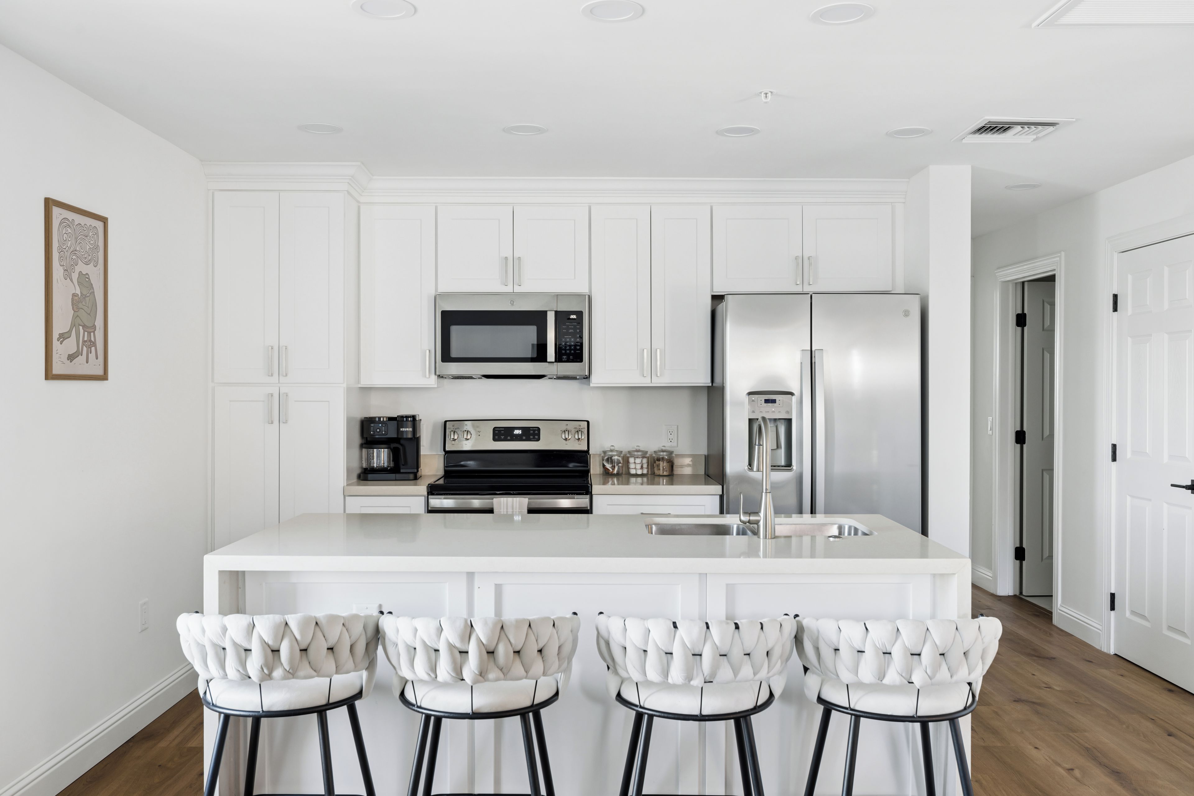Una cocina moderna con armarios blancos, electrodomésticos de acero inoxidable y una isla central con taburetes de bar.