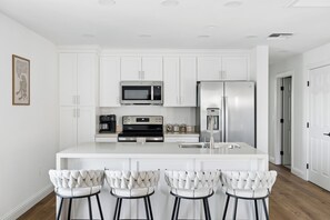 A modern kitchen with white cabinetry, stainless steel appliances, and a central island with bar stools.