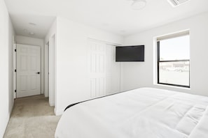 A bedroom with a bed, a TV mounted on the wall, and a window with a view of the outside.