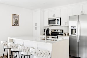 A modern kitchen with white cabinetry, stainless steel appliances, and a central island with bar stools.