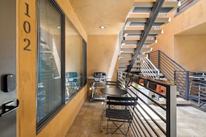 Un couloir avec un escalier, une fenêtre portant un numéro et une table avec des chaises.