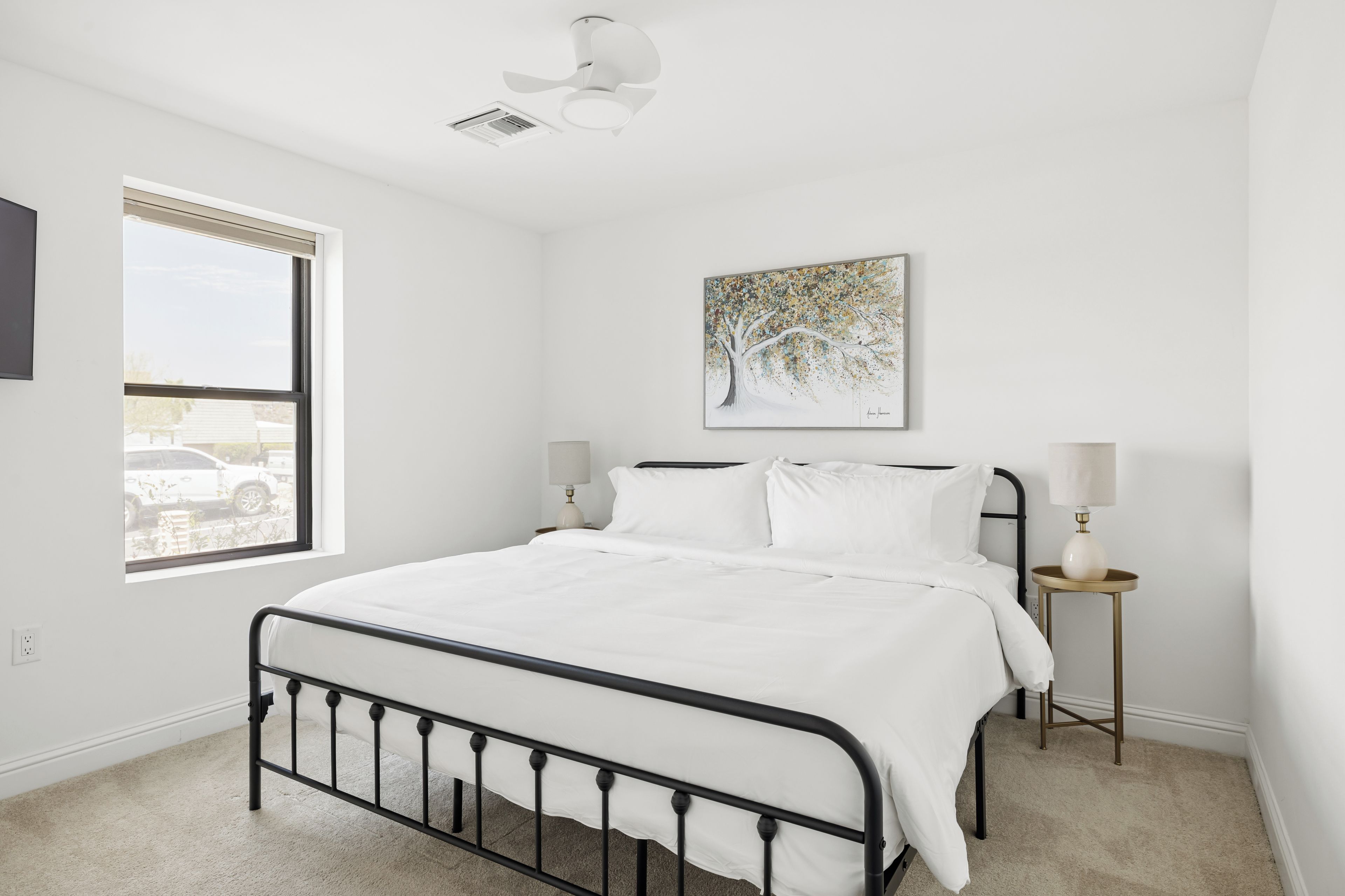 Une chambre à coucher avec un lit, une fenêtre, un ventilateur de plafond, un tableau et des lampes de chevet.