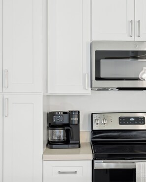 Una cocina con armarios blancos, un microondas GE, una cafetera Keurig y un horno de acero inoxidable.