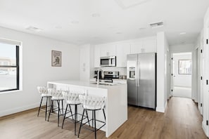 Une cuisine moderne avec des meubles blancs, des appareils en acier inoxydable et un coin bar doté de tabourets blancs.