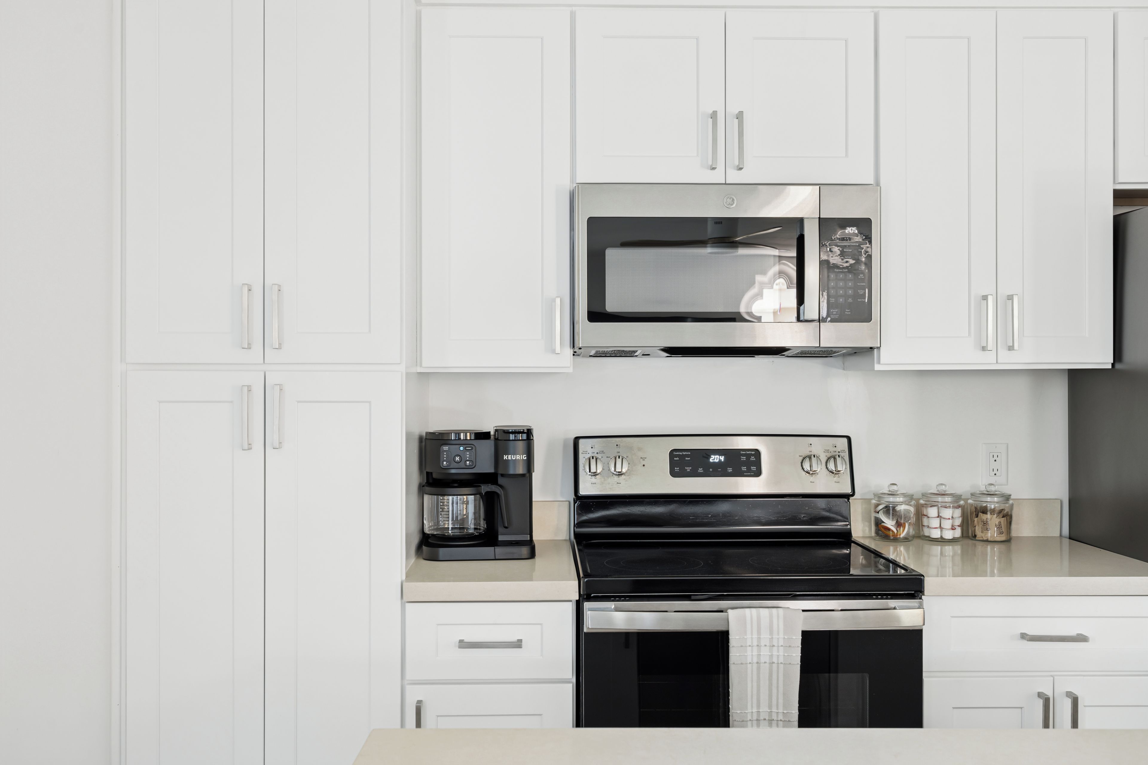 A modern kitchen with white cabinetry, a built-in microwave, a coffee maker, and a stove.