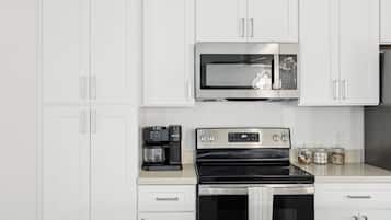 A modern kitchen with white cabinetry, a built-in microwave, a coffee maker, and a stove.