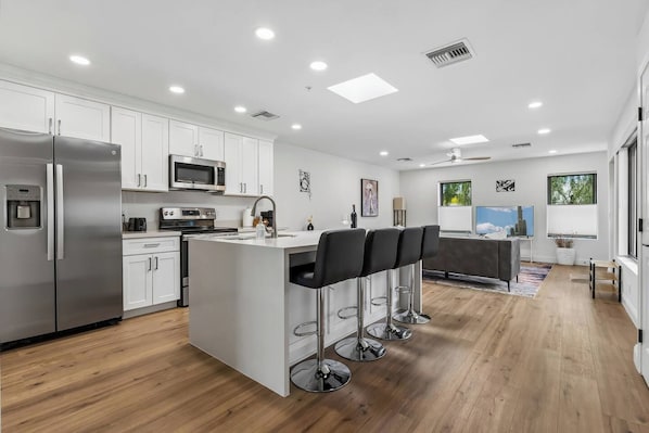 A modern kitchen with a central island, bar stools, and a dining area with a view.