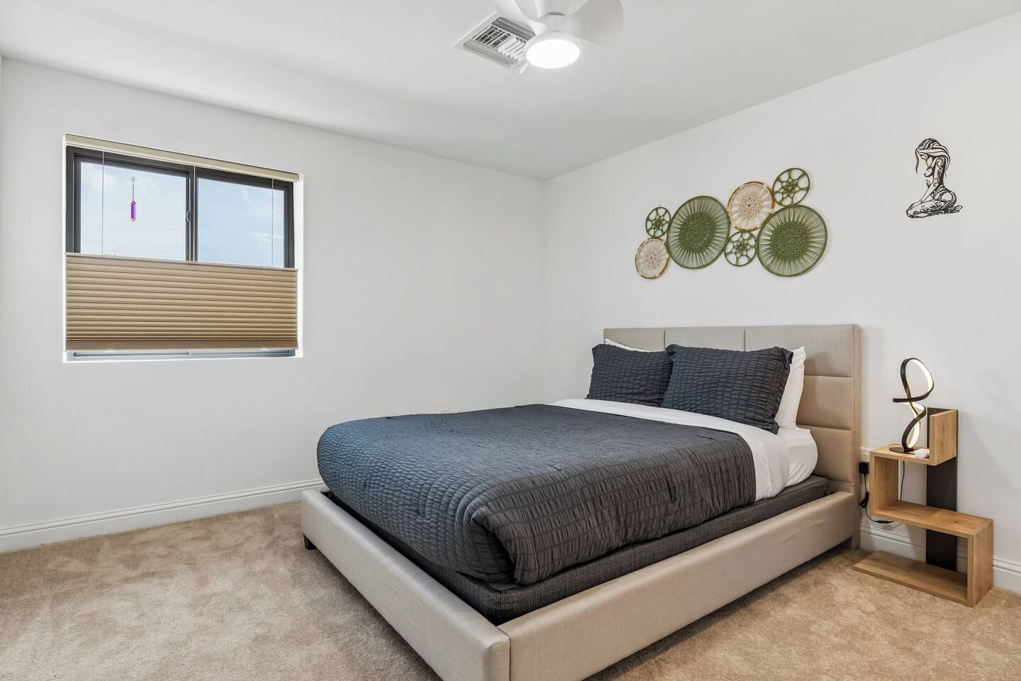 Un dormitorio con cama, ventana con persianas, ventilador de techo y decoración en la pared.