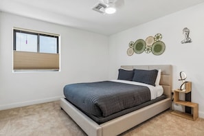 A bedroom with a bed, a window with blinds, a ceiling fan, and wall art.