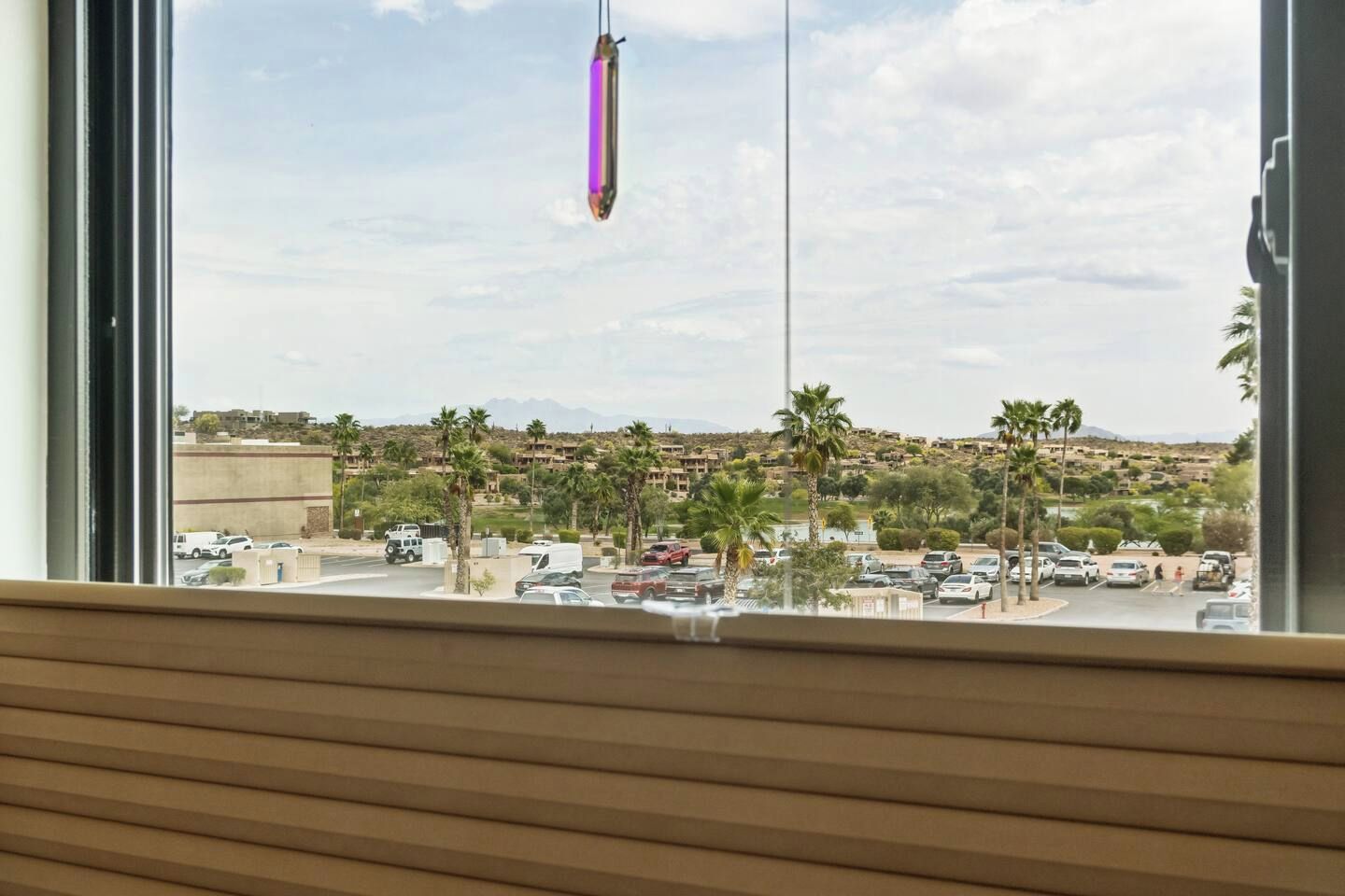 Blick aus einem Fenster auf einen Parkplatz mit Palmen und eine entfernte Hügellandschaft.
