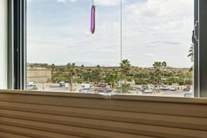 A view from a window overlooking a parking lot with palm trees and a distant hilly landscape.