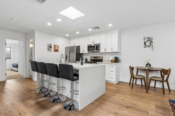 Una cocina moderna con armarios blancos, una isla central con taburetes y un comedor con sillas de madera.