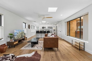 Un salon moderne avec un canapé, une table basse et un téléviseur. Il y a également un coin cuisine avec des placards et un espace repas avec des chaises.