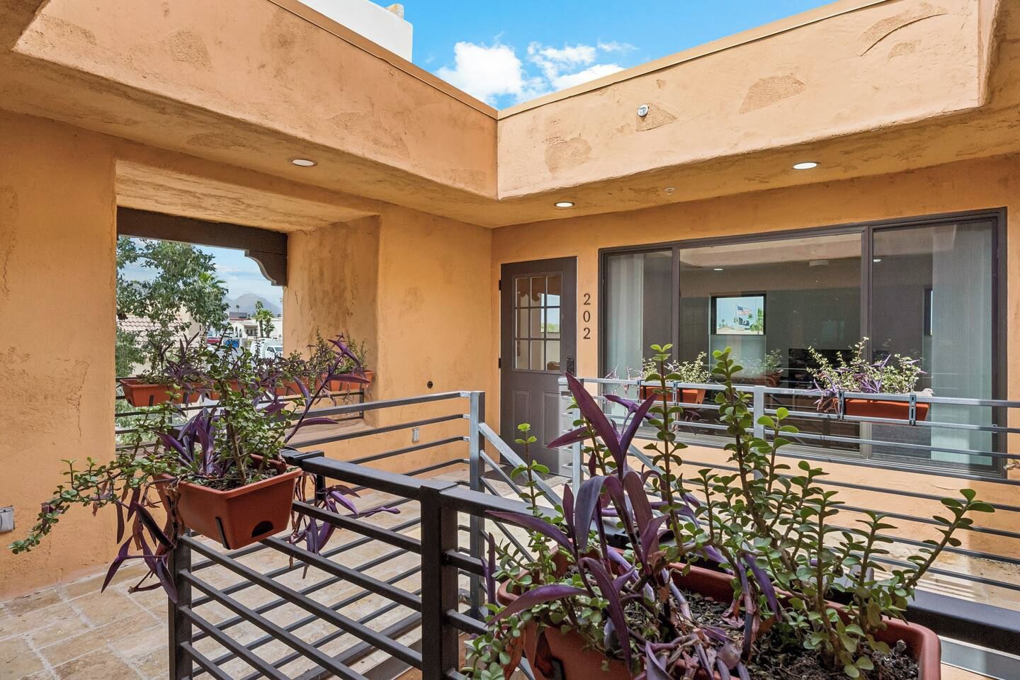 A courtyard with potted plants, a metal railing, and a building with a glass door.