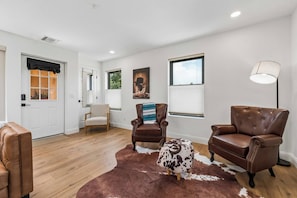 Un salon spacieux doté d’un plancher en bois, de fauteuils en cuir, d’un tapis en peau de vache et d’un tableau accroché au mur.