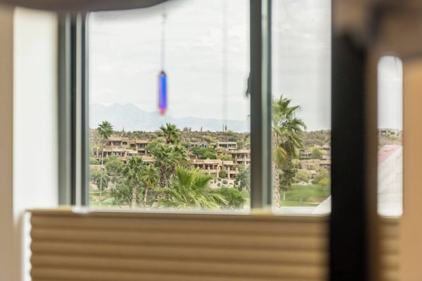 Une vue à travers la fenêtre d’un immeuble doté de nombreux balcons, de palmiers et d’une chaîne de montagnes lointaine.