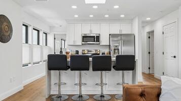 Cocina moderna con armarios blancos, electrodomésticos de acero inoxidable y una zona de bar con cuatro taburetes.