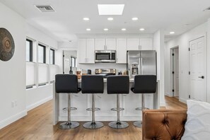 A modern kitchen with white cabinets, stainless steel appliances, and a bar area with four stools.