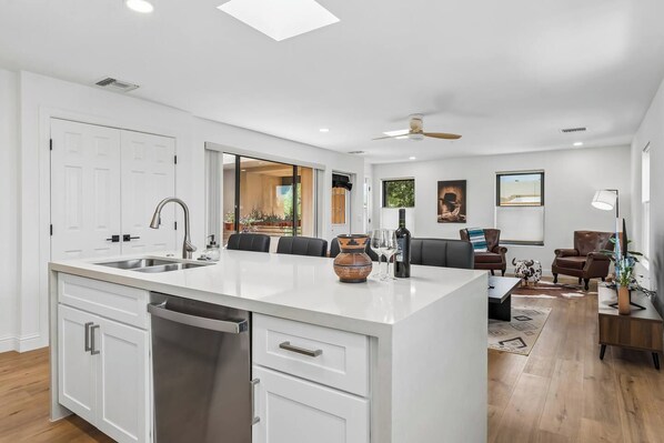 A modern kitchen with a central island, a dining area with a sofa and chairs, and a living room with a TV and a lamp.