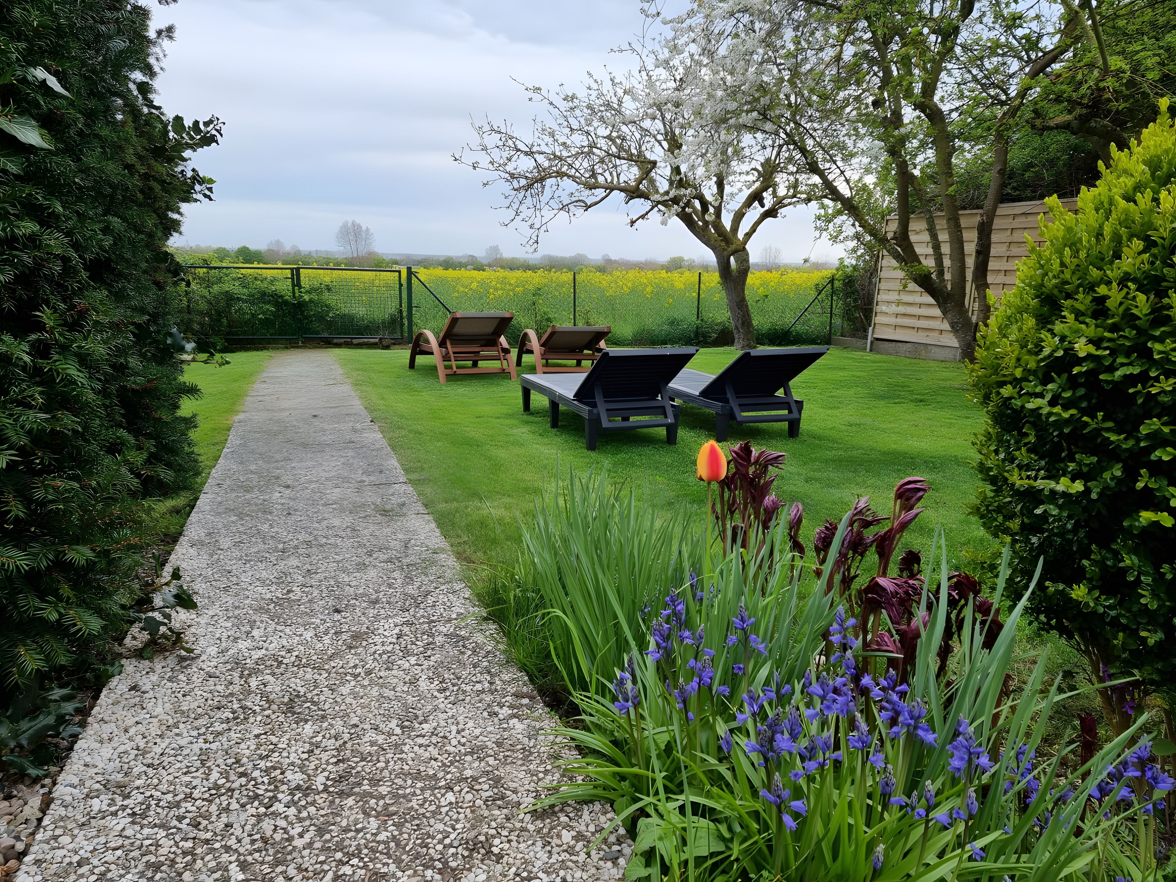 Un giardino con vialetto in ghiaia, poltrone da relax e piante fiorite.
