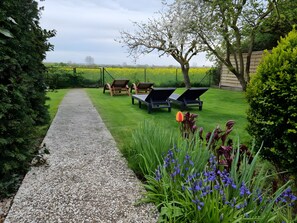 A garden with a gravel path, lounge chairs, and flowering plants.