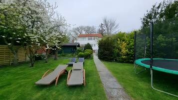 Un patio trasero con un trampolín, dos sillones de descanso, un sendero y una casa al fondo.
