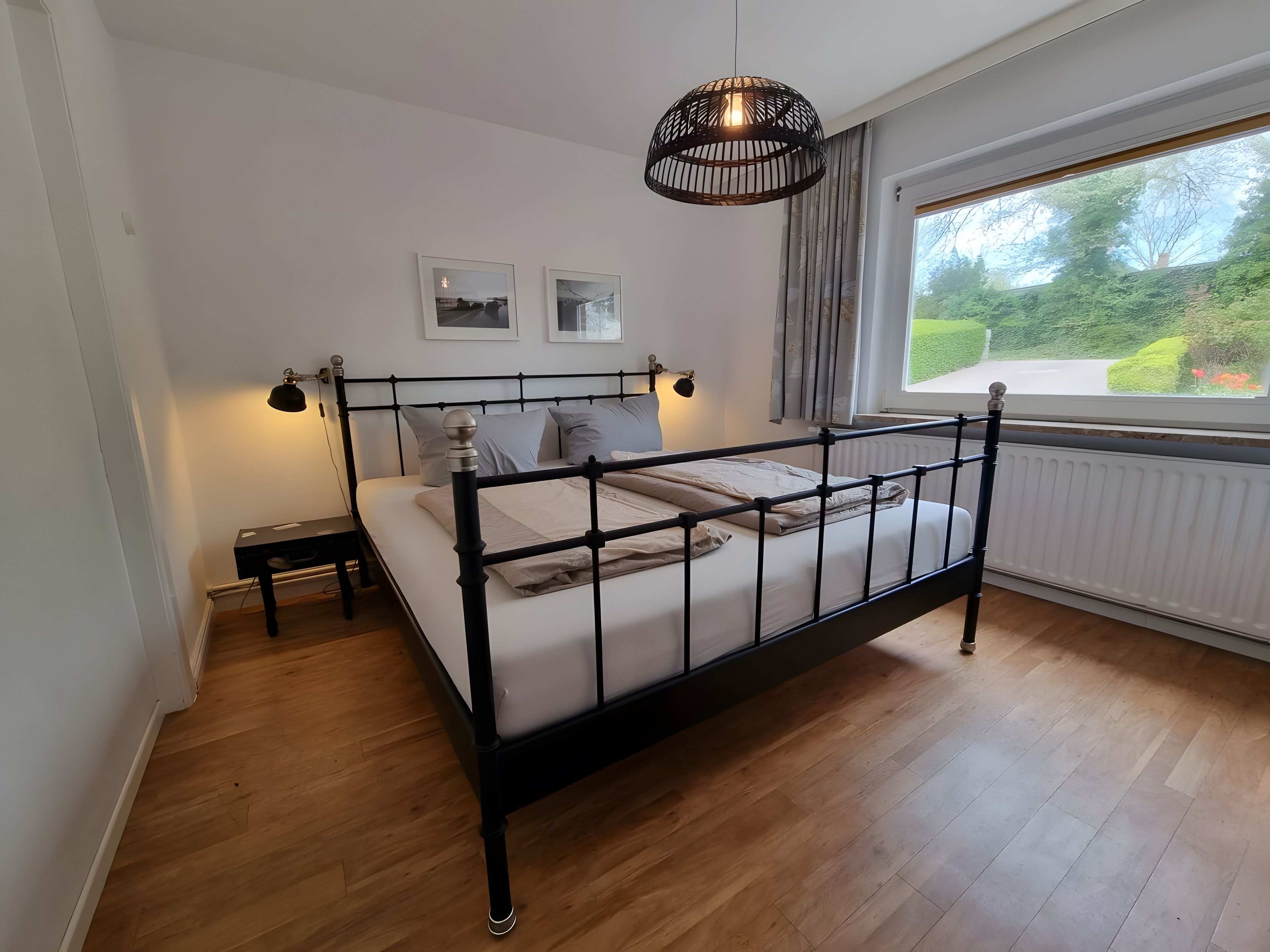 Un dormitorio con cama, lámparas de noche, ventana con vistas y radiador.