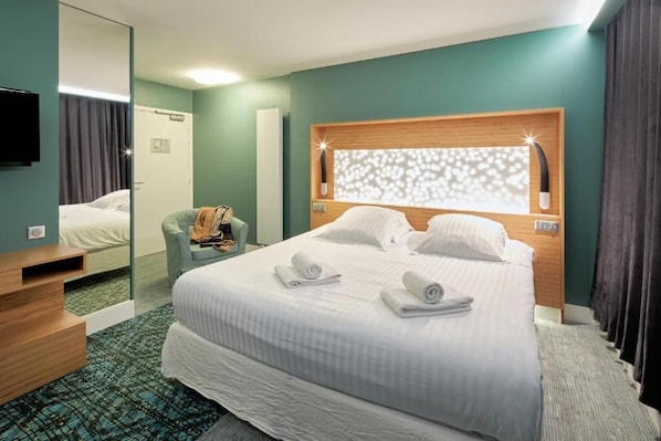 A hotel room with a bed, a mirror, a chair, and a television.