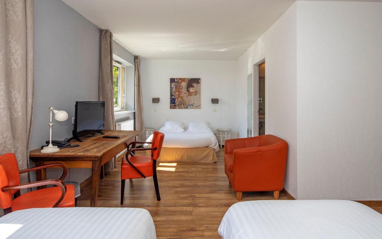 Une chambre d’hôtel avec un lit, un bureau avec un ordinateur, deux chaises et un tableau au mur.