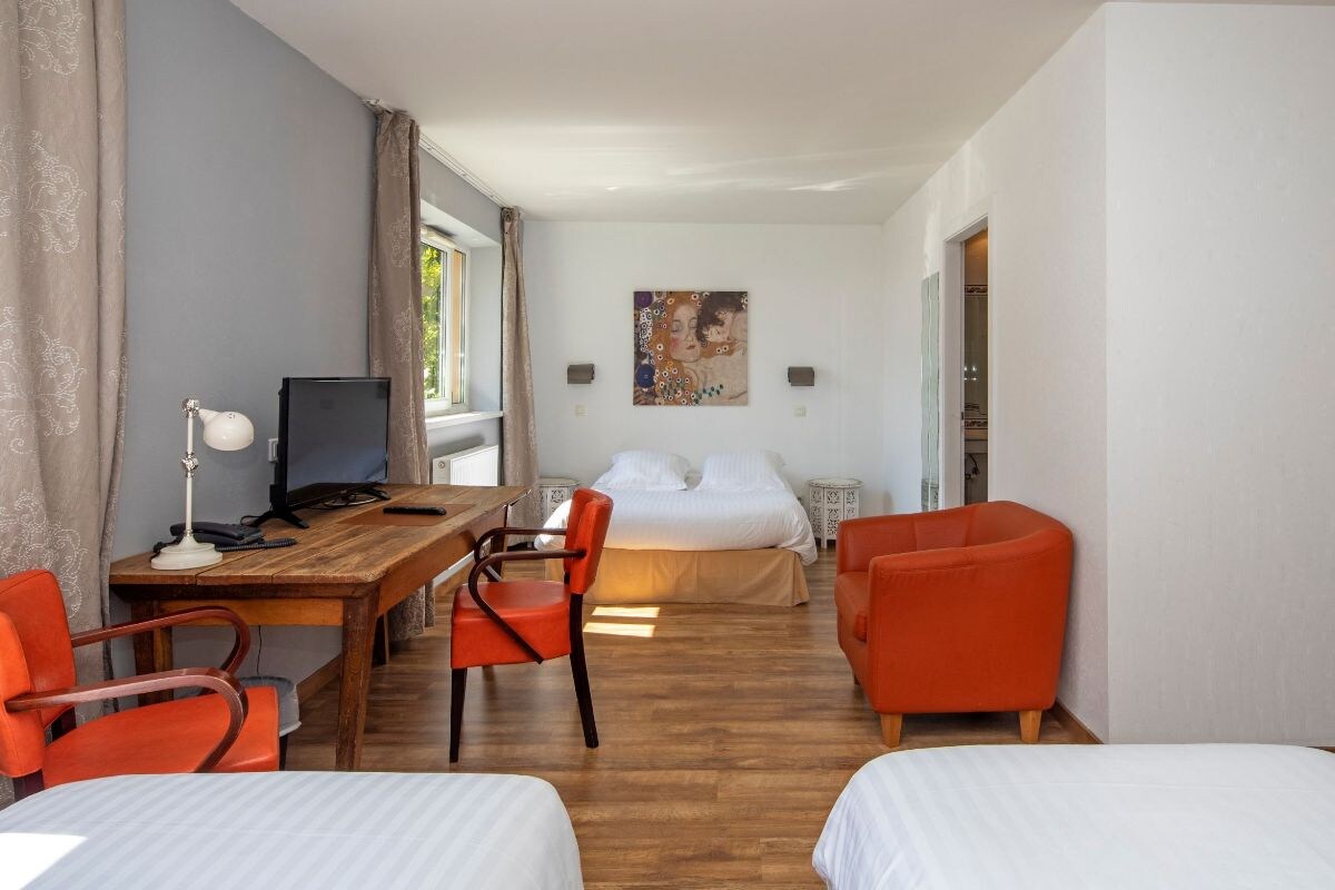 Een hotelkamer met een bed, een bureau met een computer, twee stoelen en een schilderij aan de muur.