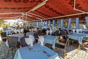 An outdoor dining area with tables set for guests, featuring wicker chairs and blue tablecloths.