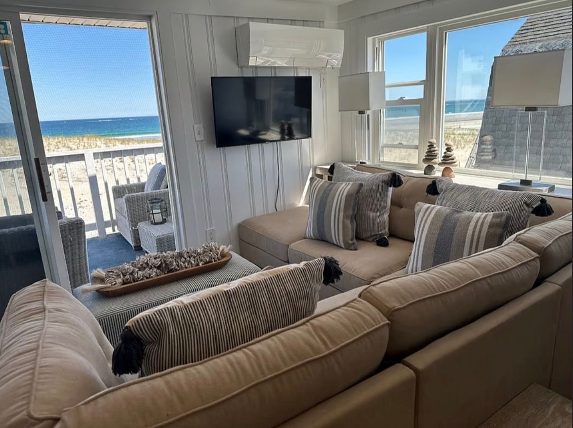 A beachside living room with a large sofa, a flat-screen TV, and a view of the ocean.