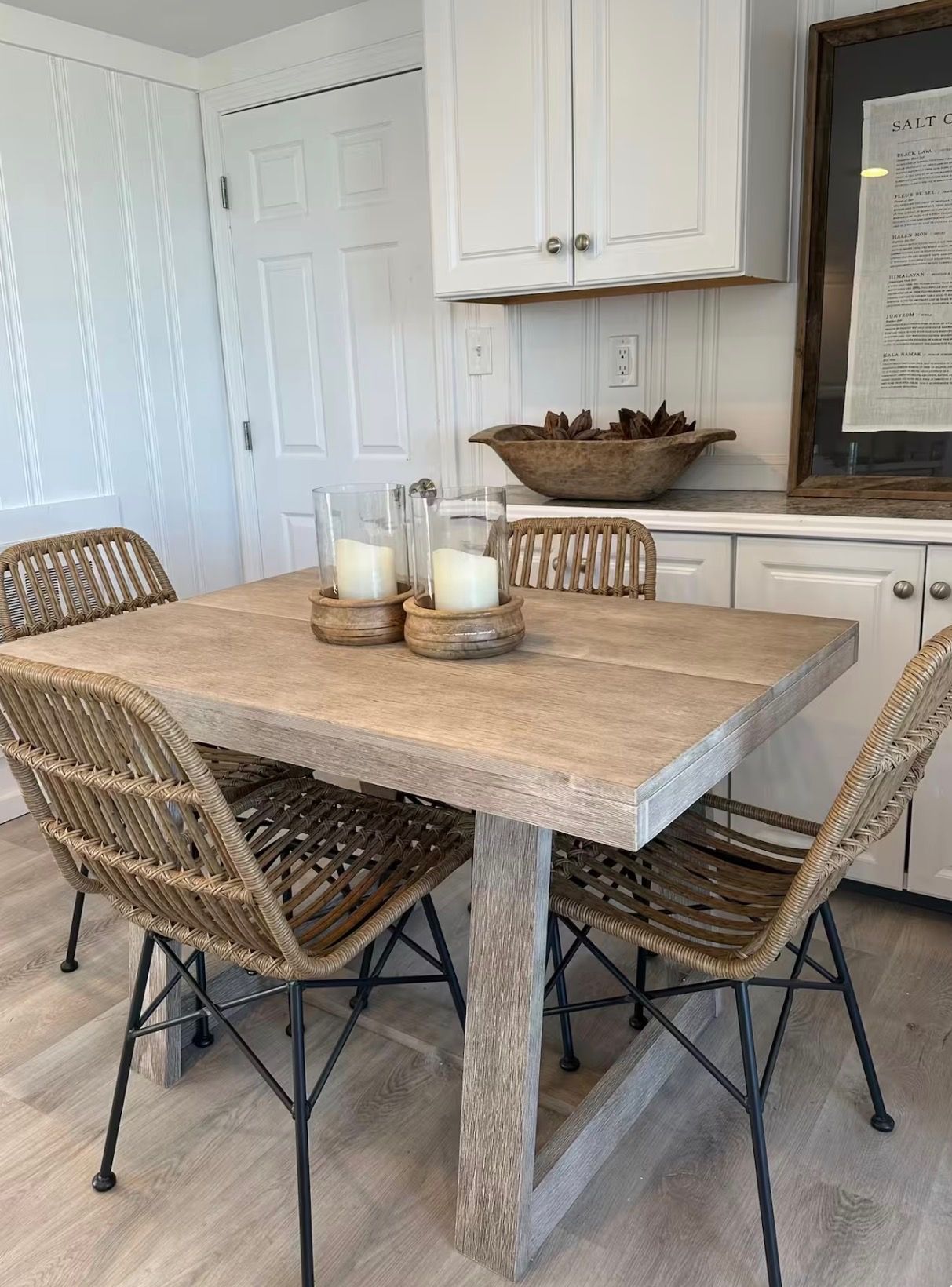 Un coin repas avec une table en bois, des chaises en osier et un saladier de fruits posé sur le comptoir.