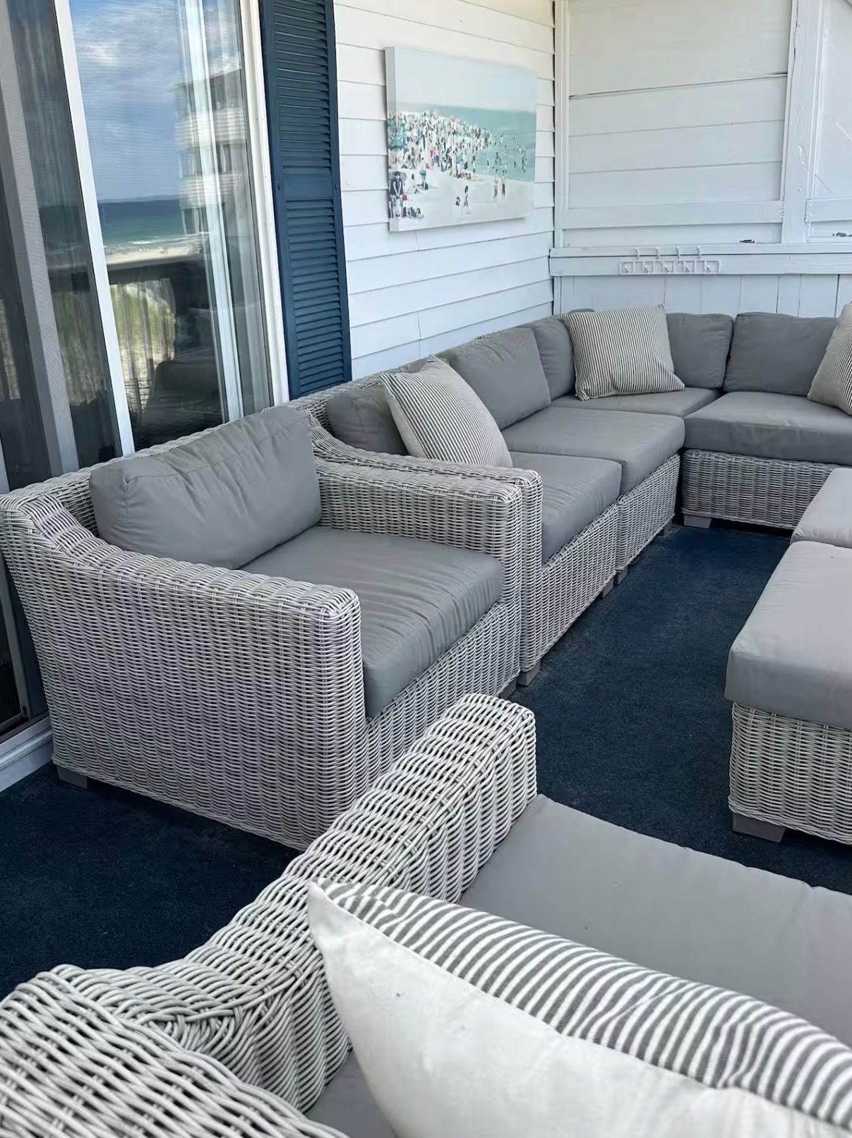 A sectional sofa with a woven design and neutral cushions, positioned on a dark carpet in a room with a view of the ocean through a glass door.