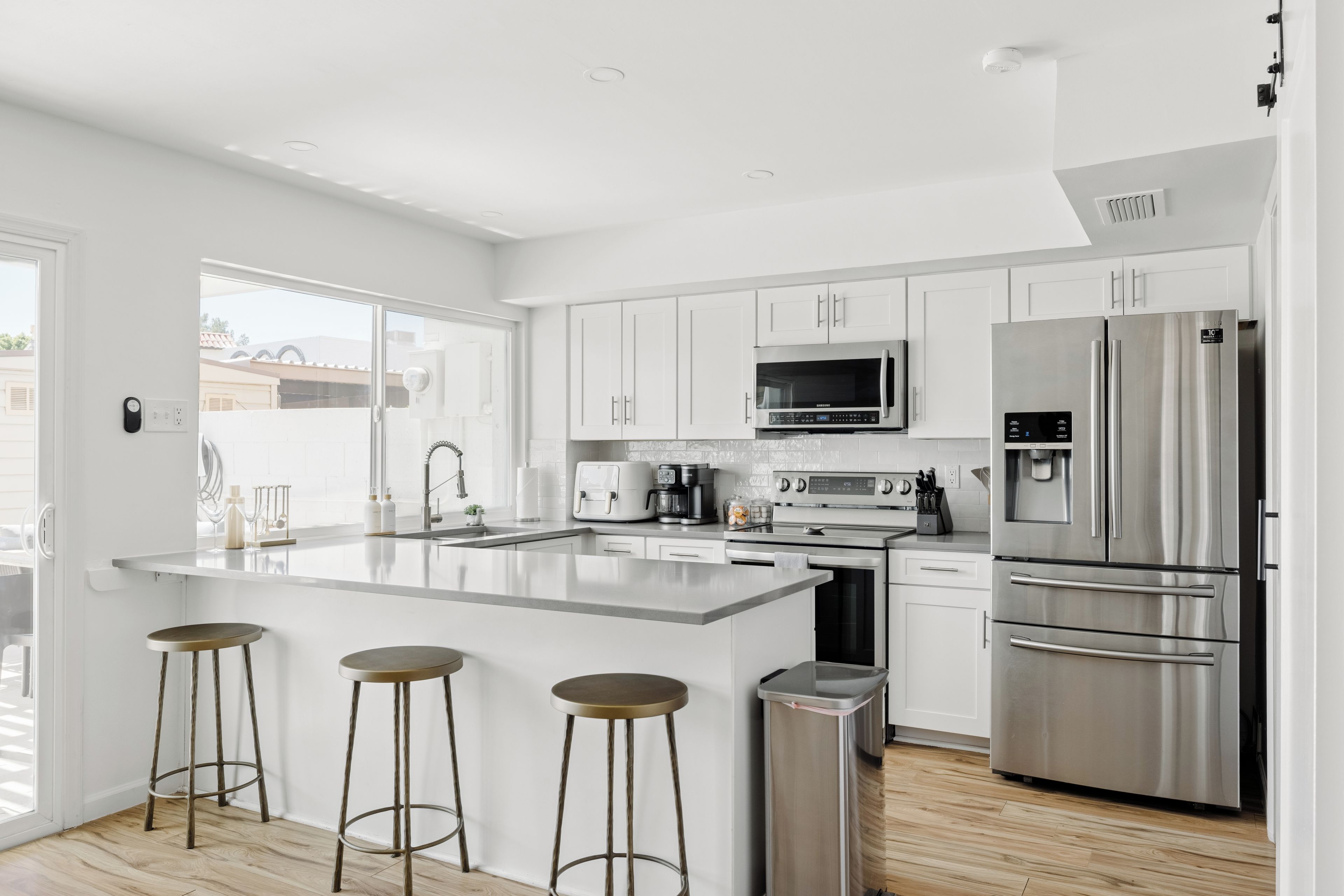 A modern kitchen with white cabinetry, stainless steel appliances, and a central island with stools.