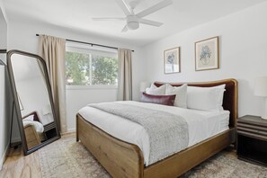 A bedroom with a wooden bed, a ceiling fan, a window with curtains, and two framed botanical prints on the wall. - Sol & Stone: Old Town Condo with Hot Tub & EV (Scottsdale)
