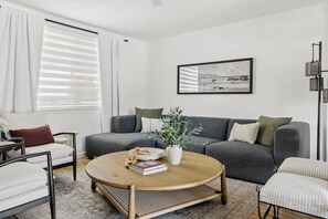 A modern living room with a grey sofa, a round coffee table, and a bookshelf. - Sol & Stone: Old Town Condo with Hot Tub & EV (Scottsdale)