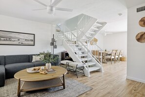 A modern living room with a white spiral staircase, a grey sofa, a round coffee table, and a dining area with wooden chairs. - Sol & Stone: Old Town Condo with Hot Tub & EV (Scottsdale)