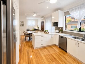 A modern kitchen with a central island, built-in appliances, and a large window with a view. - Cosy Sunlit home with a Pool (Smithfield)