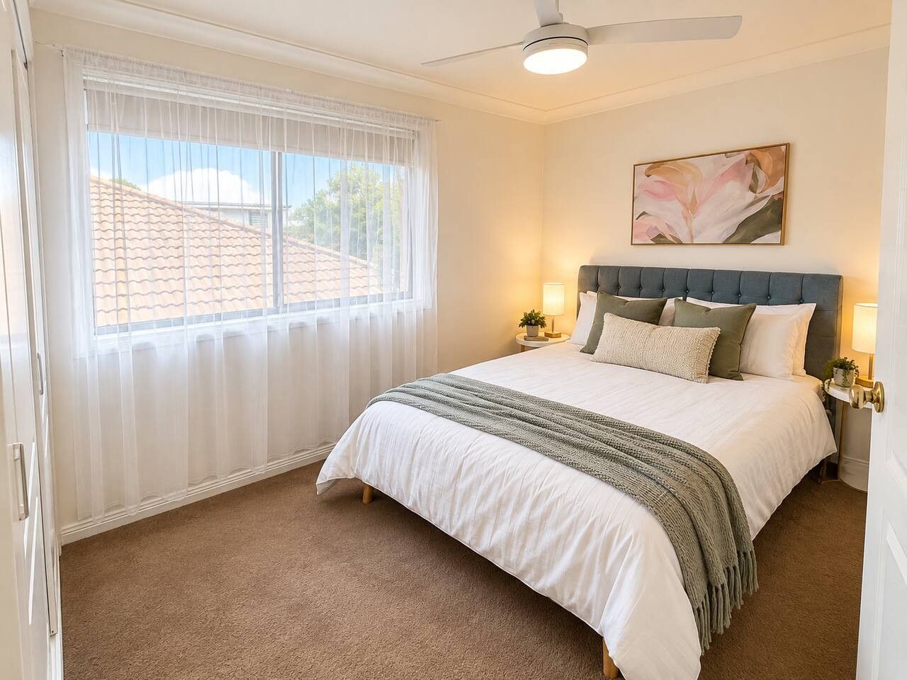 A bedroom with a bed, a ceiling fan, a window with curtains, and a wall-mounted lamp.