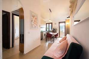 A living room with a sofa, a dining area with a table and chairs, a kitchen with a washing machine, and a hallway with a door. - Cactus Apartments. 200 meters from the beach. Ocean view. (Solanas)