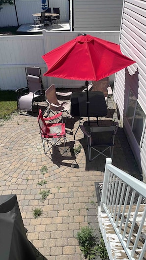Eine Terrasse im Freien mit Grill, Klappstühlen und einem roten Sonnenschirm.