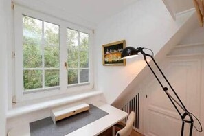 A room with a desk, a standing lamp, and a window with a view of greenery. - Ameland Reethus (Wenningstedt) (Wenningstedt-Braderup)